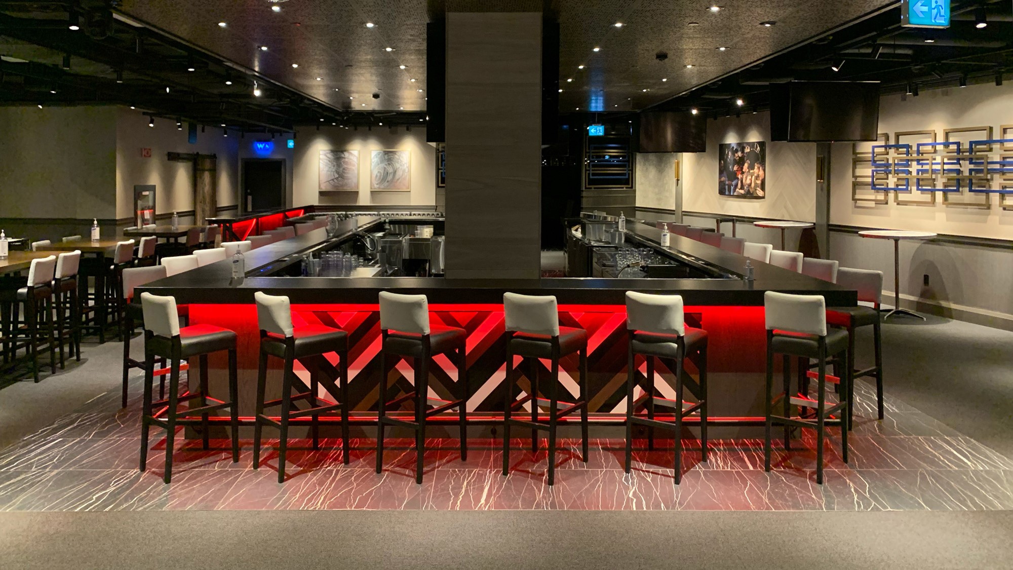 Modern bar with high-backed chairs and a red-lit counter in a dimly lit space.