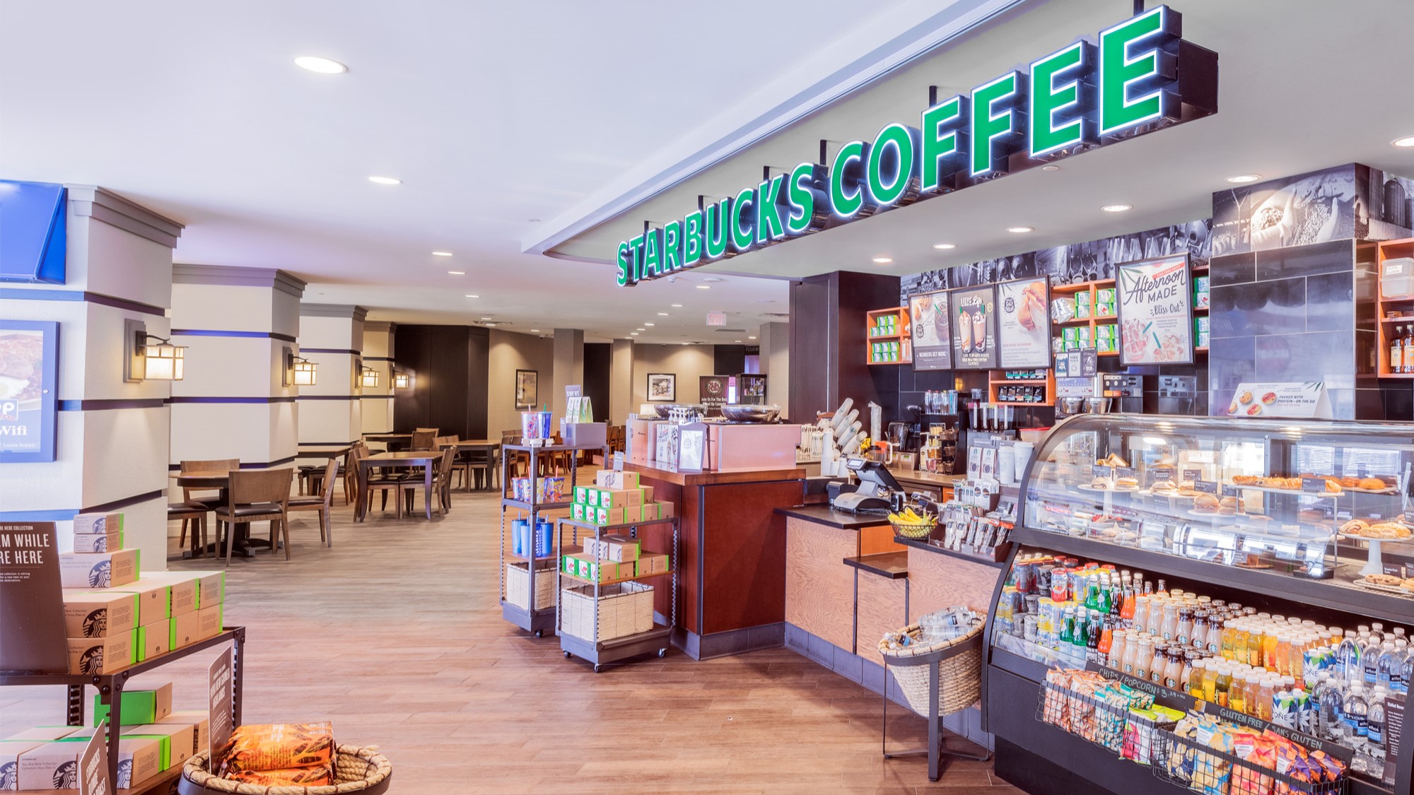 Starbucks café in lobby with a well-lit seating area, a counter displaying food and drinks, and shelves stocked with coffee products.