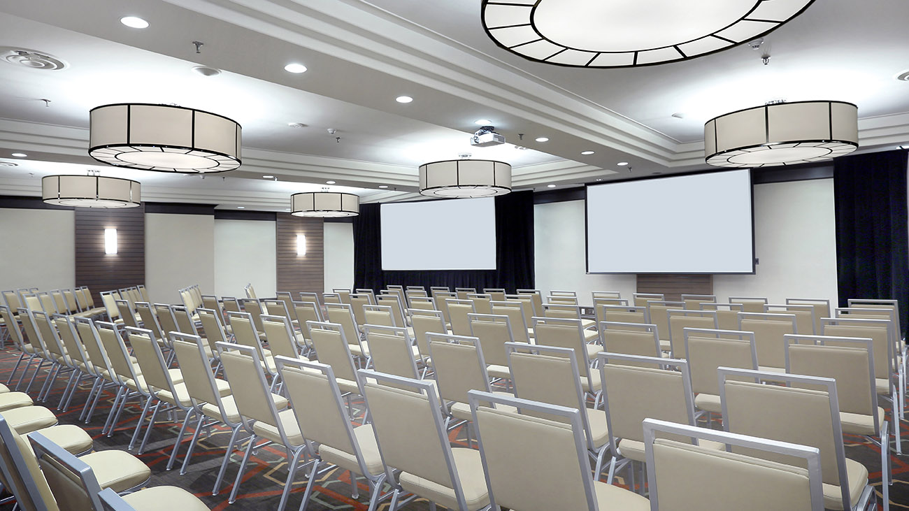 An expansive conference room equipped with multiple rows of chairs and a prominent projector screen for visual displays.