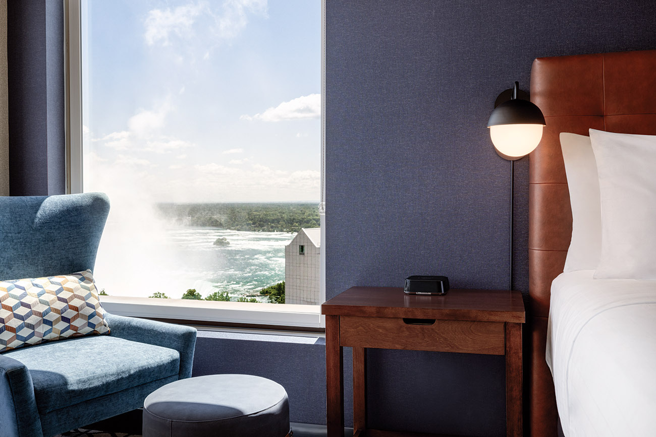 A well-furnished hotel room with a chair in front of a picturesque view of the falls, perfect for unwinding.