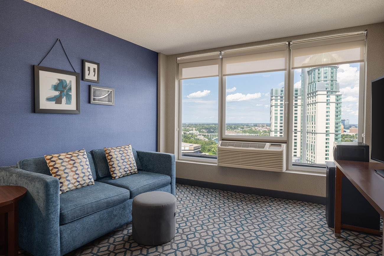 A sitting room with a couch located just off the bedroom, offering a stunning view of the city skyline through large windows.