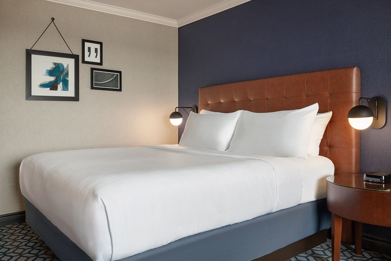 An inviting hotel room with a plush king bed, a bedside nightstand, and artistic pictures displayed on the walls.