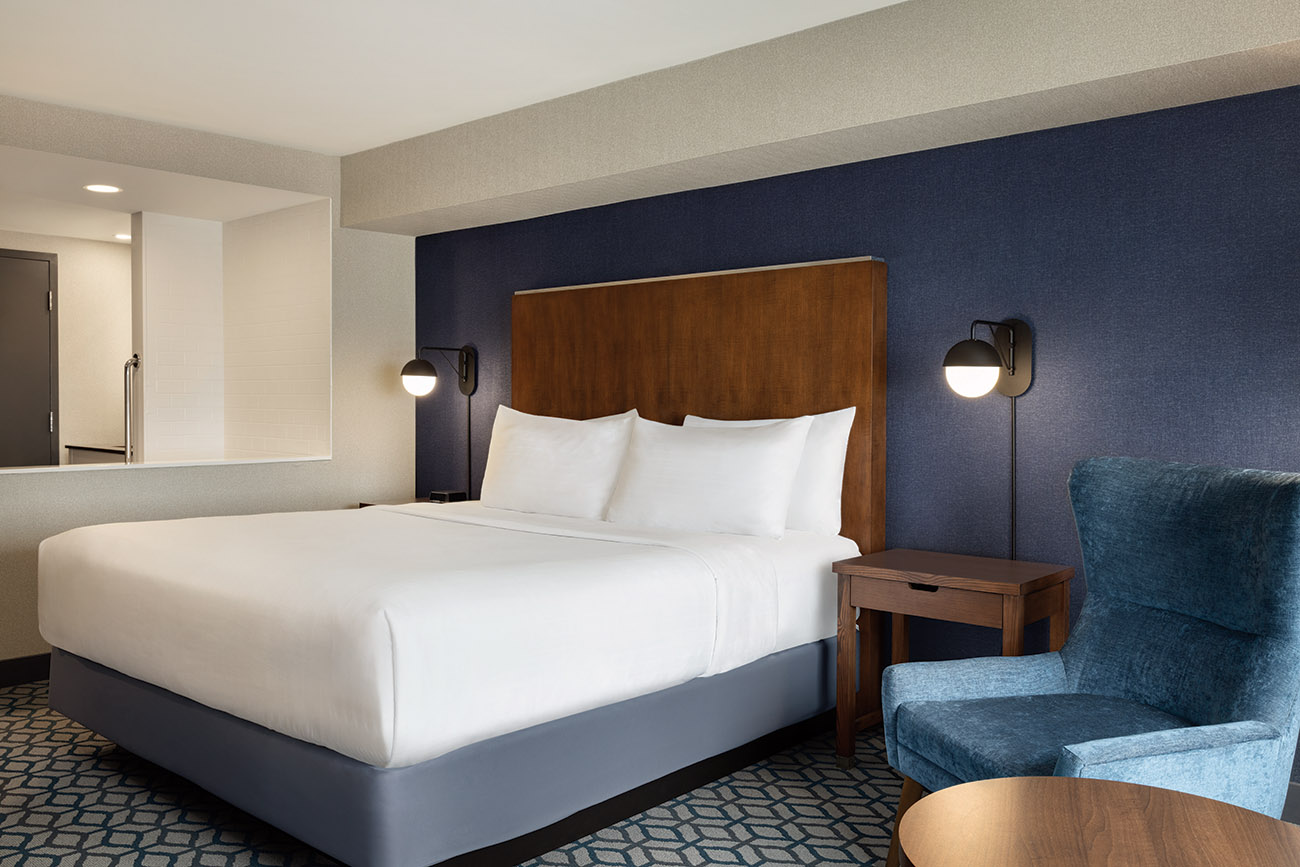 An inviting hotel room with a plush king bed, a bedside nightstand, and an inviting jacuzzi tub for relaxation.