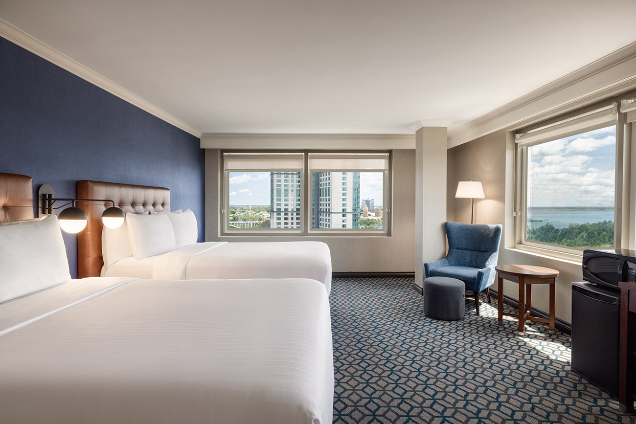 A hotel room featuring two beds, a television, and large windows allowing viewing Niagara Falls.